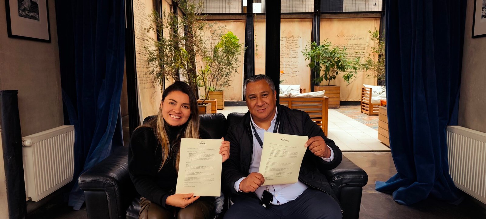 Dos ejecutivos sonrientes sostienen documentos firmados en el patio interior de un hotel en Viña del Mar