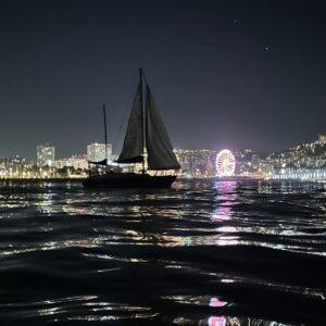 Yate a vela nocturno frente al skyline y noria de la bahía